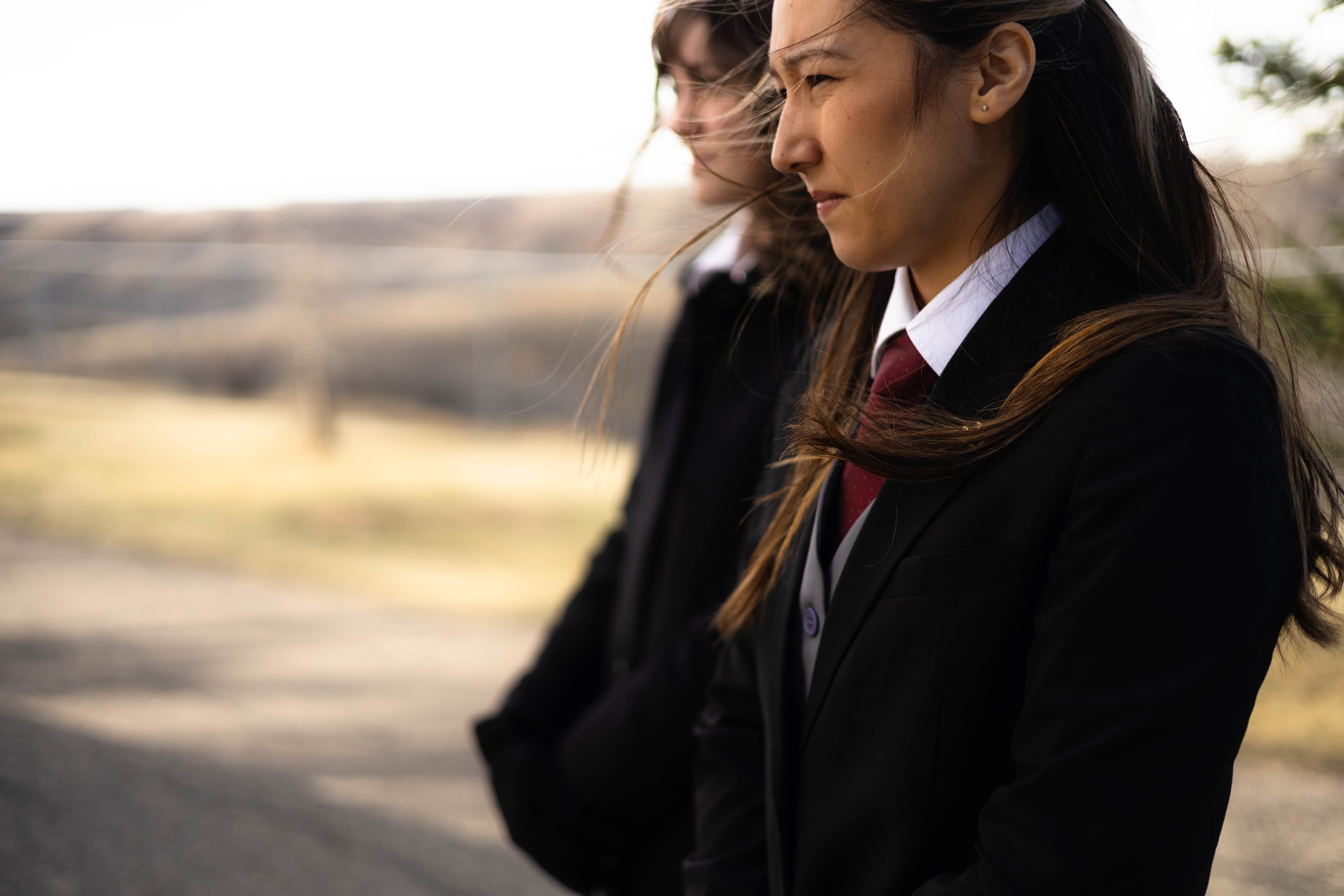 A cinematic medium-close portrait of two funeral professionals in formal black suits and ties. Standing against a blurred Southern Alberta coulee landscape, their expressions are composed and resolute, reflecting a high standard of professional presence and stewardship.